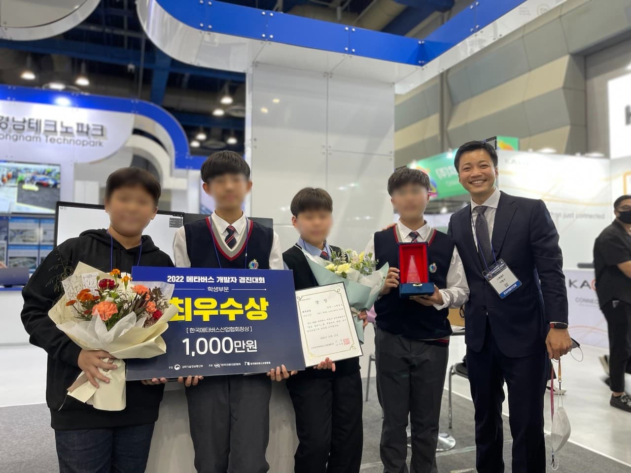 2022 메타버스 개발자 경진대회 학생부문 최우수상 시상 후 학생 네 명과 원장이 상패와 꽃다발을 들고 선 사진. 학생 얼굴은 흐리게 가렸다